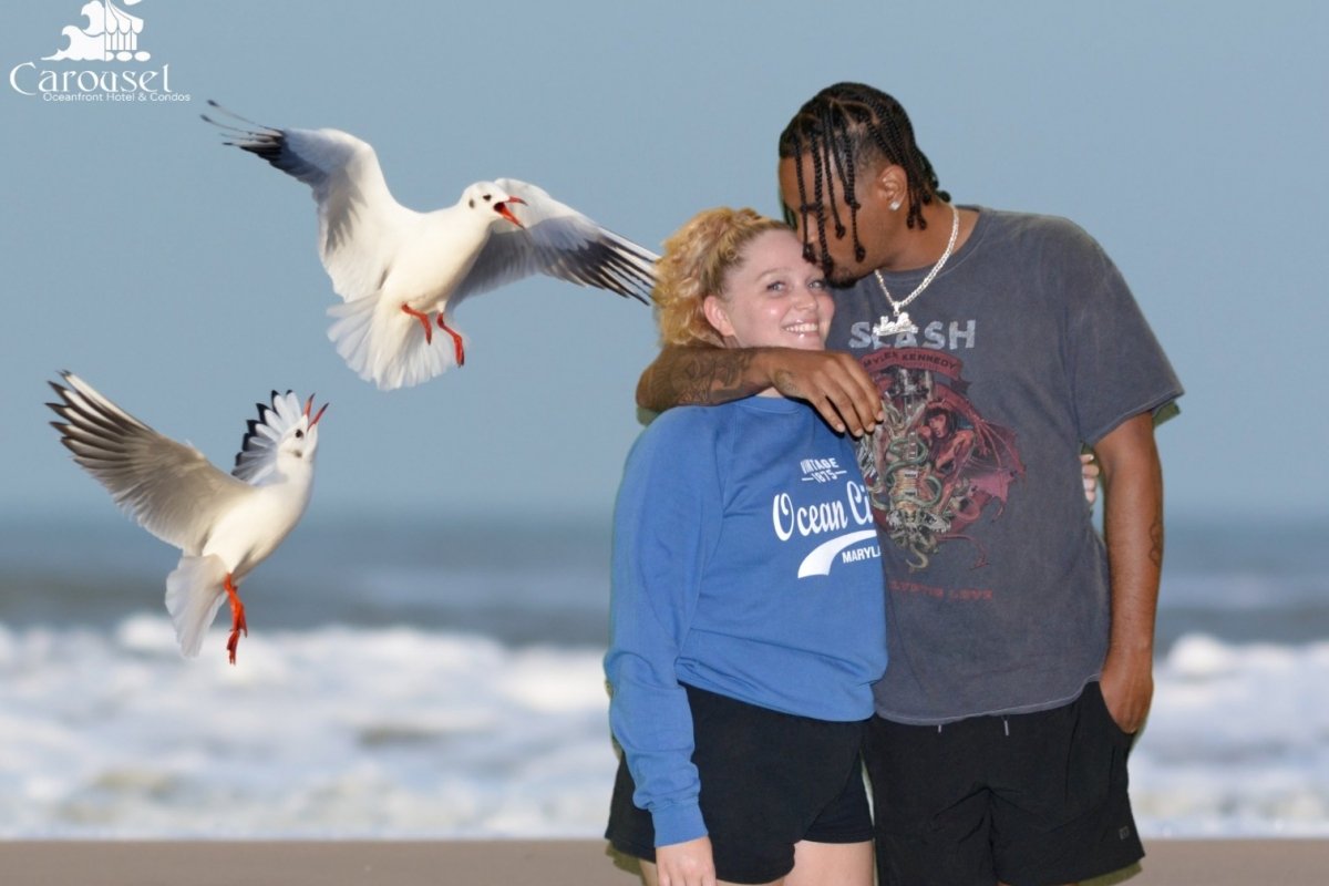 A couple posing in front of the ocean with seagulls behind them.