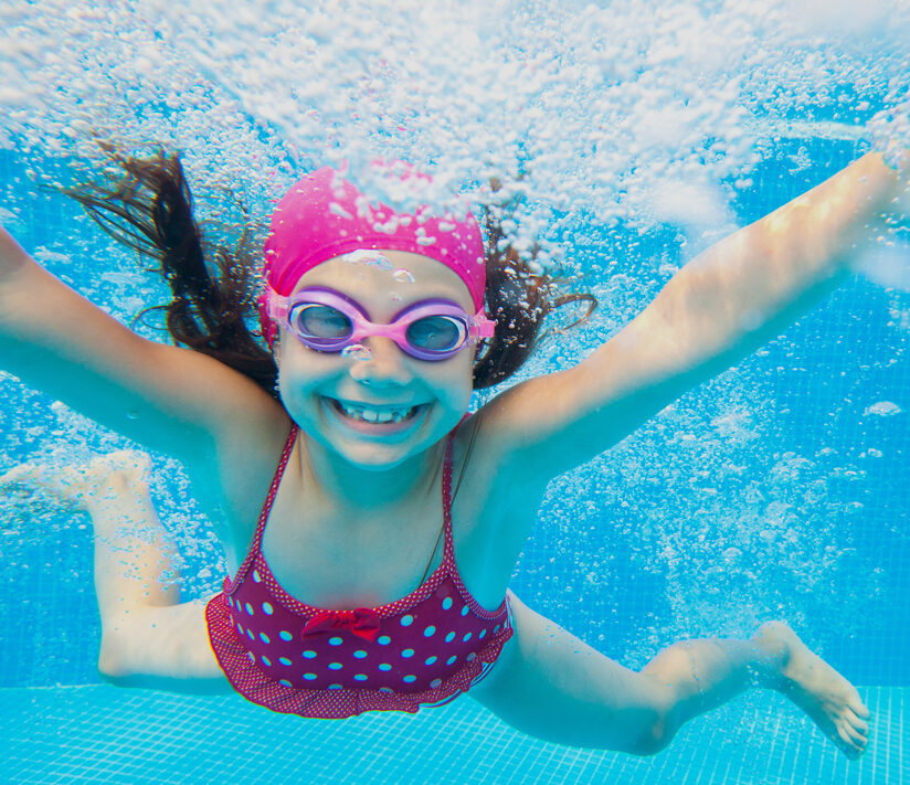 A girl swimming in the pool with goggles.