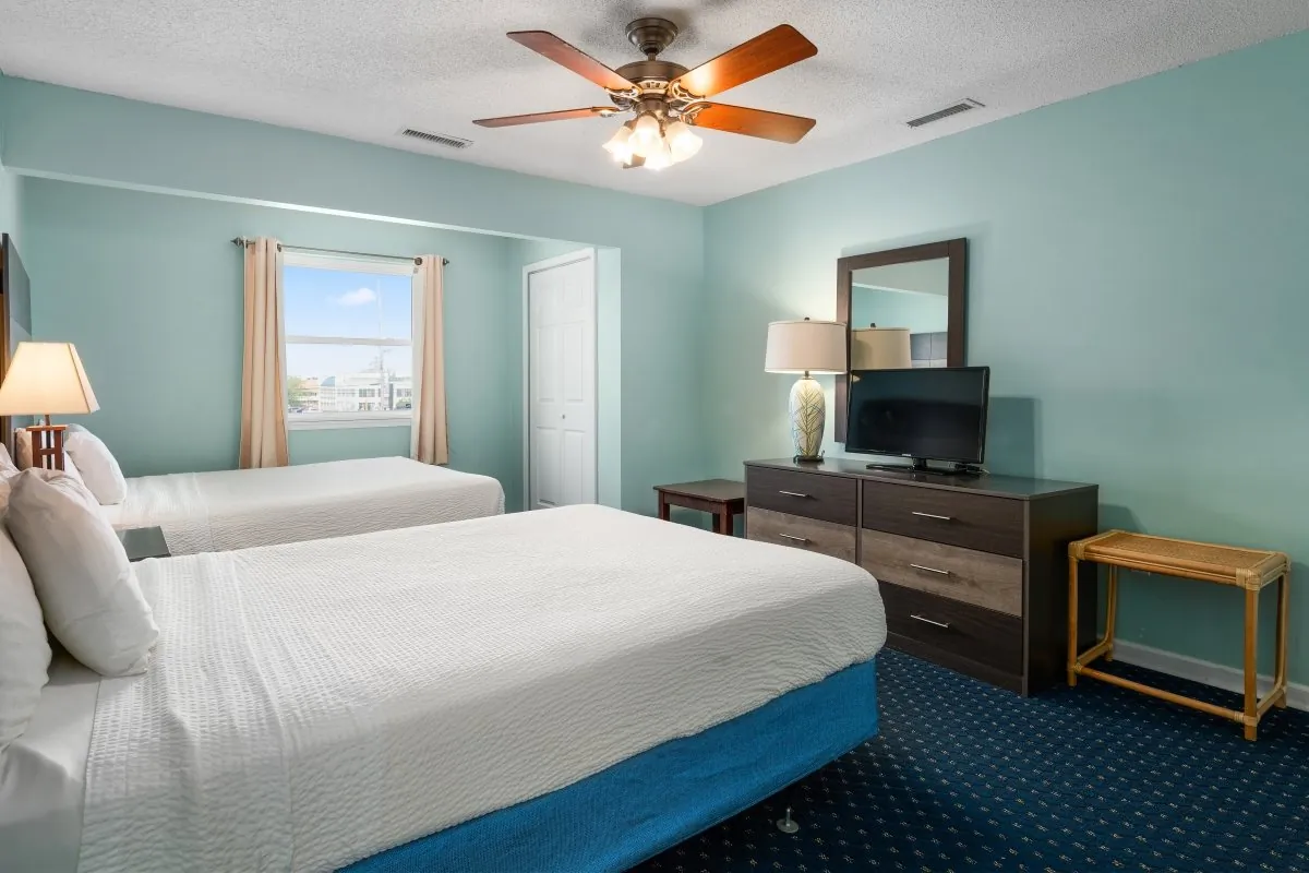 A hotel room with two beds, a tv, a dresser and other furniture.