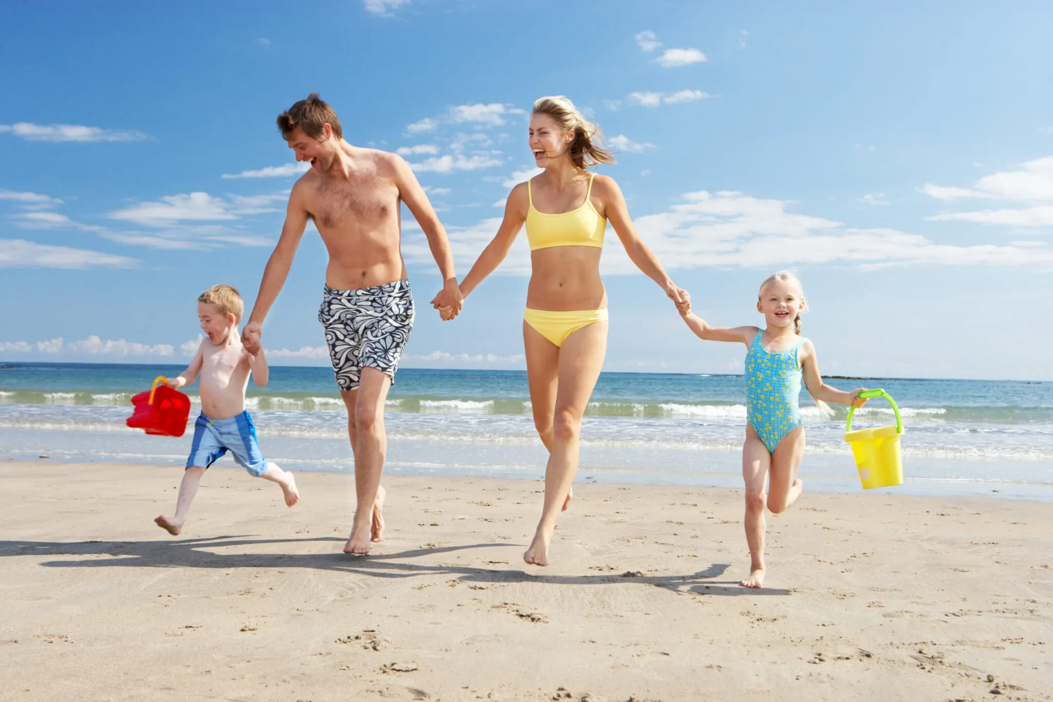 A family of four walks along the beach, with the ocean in the background.