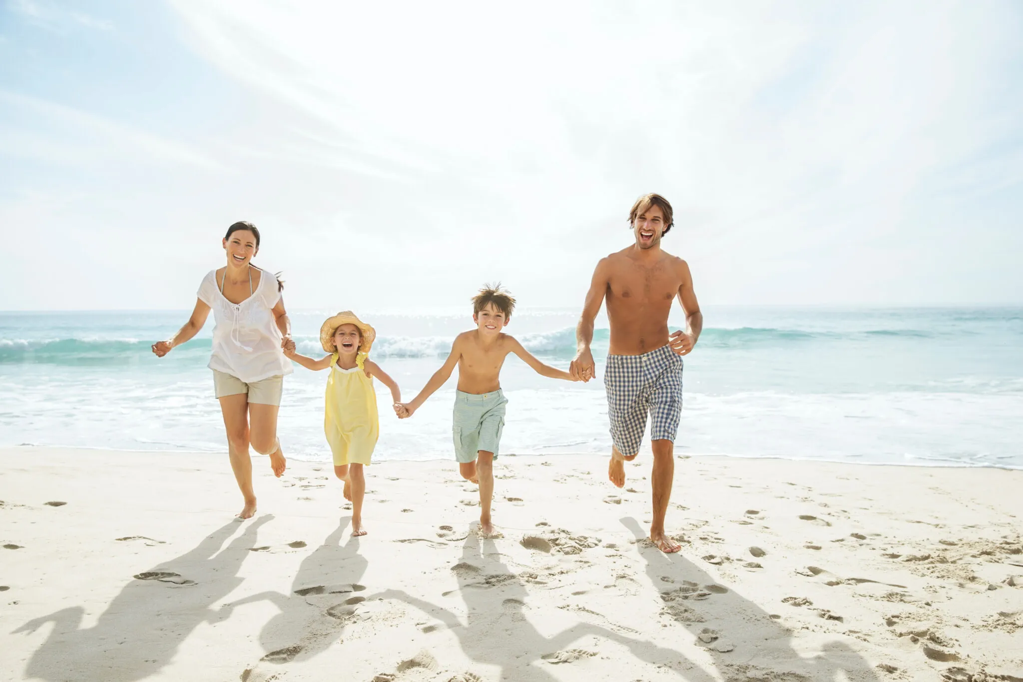 A family of four runs along the beach with the ocean in the background.