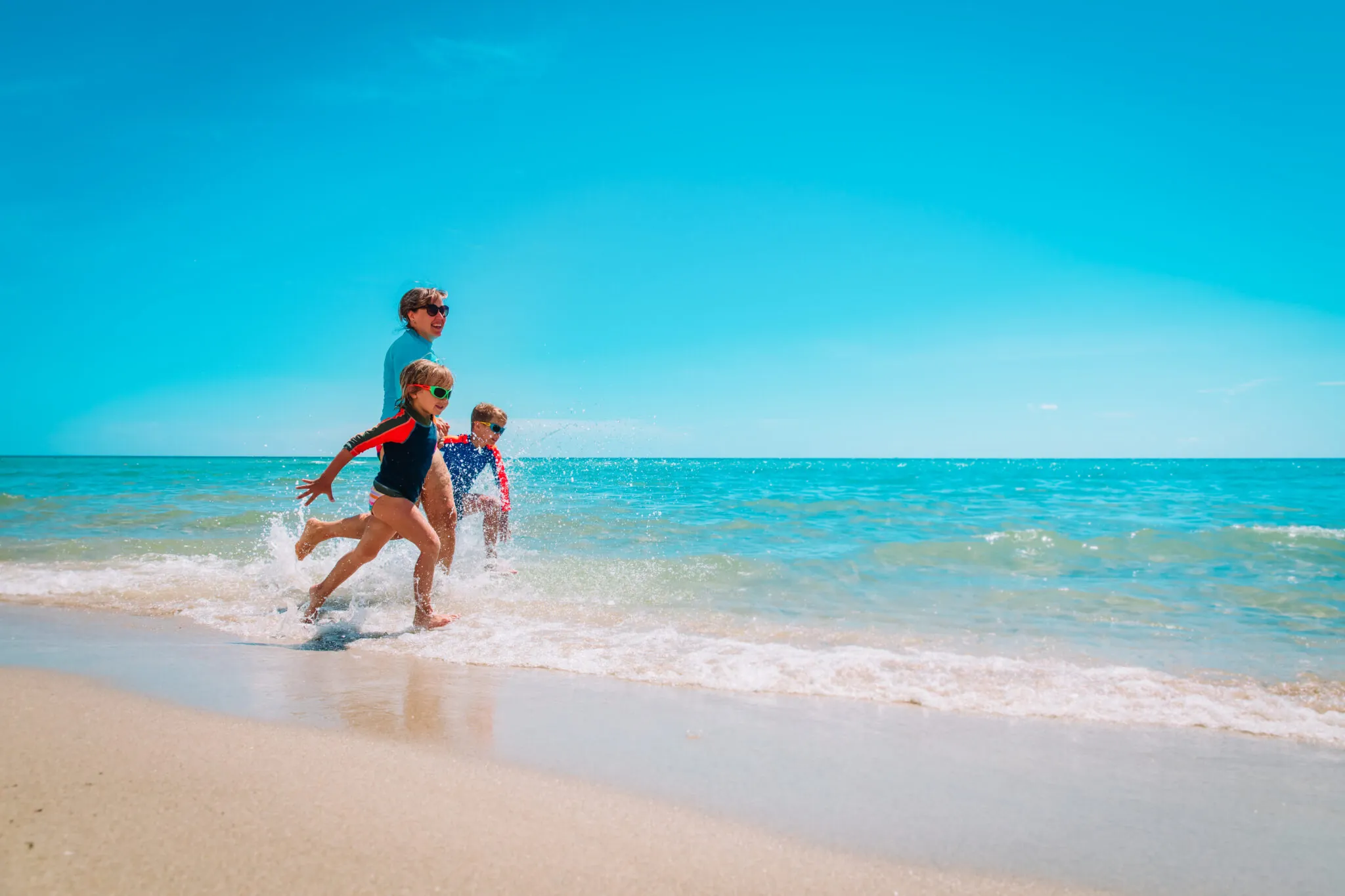 A family of three runs along the beach with waves crashing at their feet.